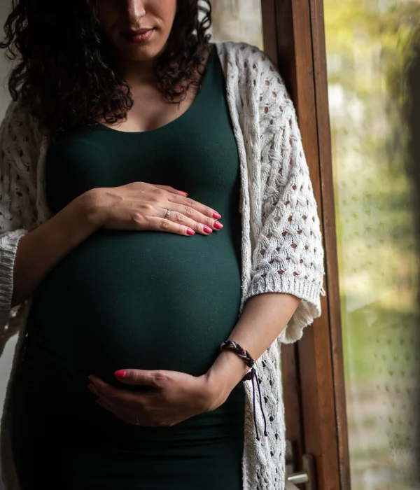 A pregnant woman stands near a window.