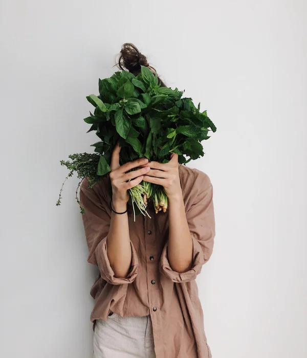 A woman covers her face with a bunch of herbs.